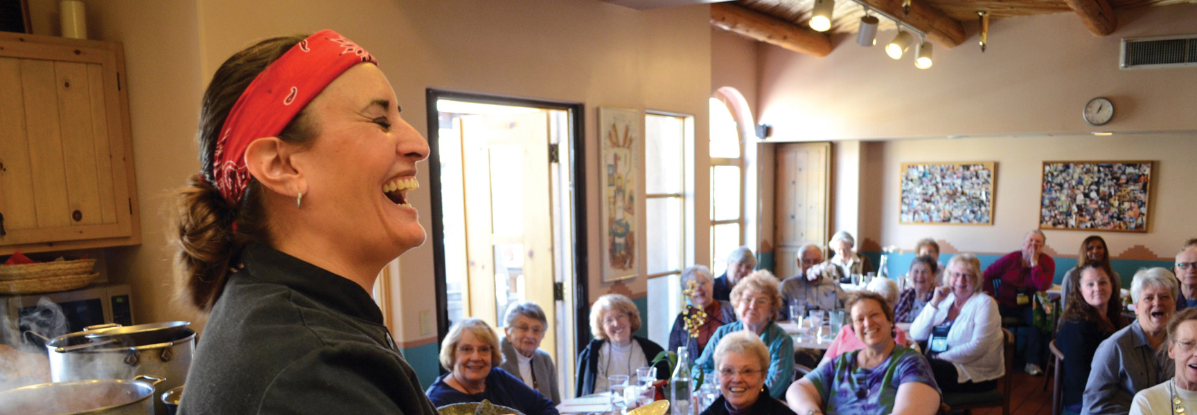 A chef wearing a red bandana laughs while leading a cooking demonstration for a large, joyful group of women in New Mexico.