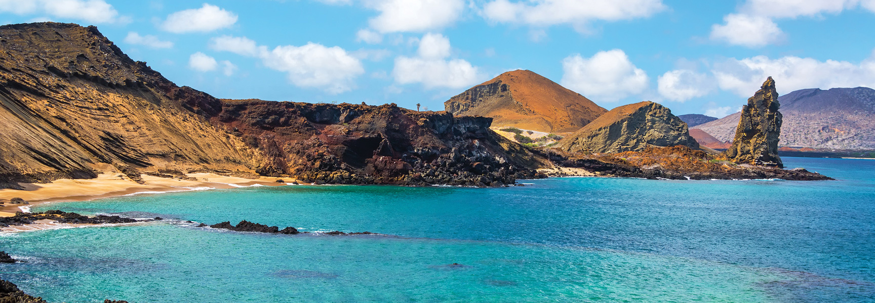 The dramatic, colorful volcanic coastline and turquoise bay of the Galápagos Islands, Ecuador, on a sunny day.