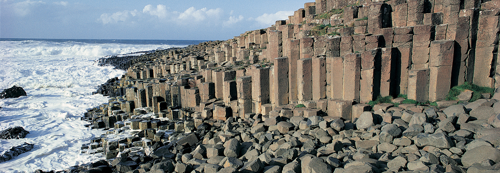 Interlocking basalt columns of the Giant's Causeway on the coast of Northern Ireland with waves crashing on the shore.