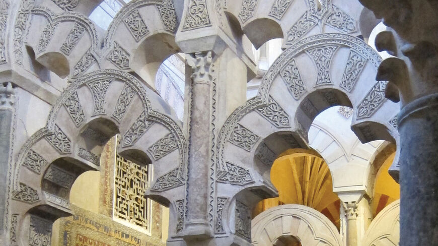 Intricate Moorish architecture in Spain featuring ornate multi-lobed stone arches with decorative carvings in a historic southern coast interior.