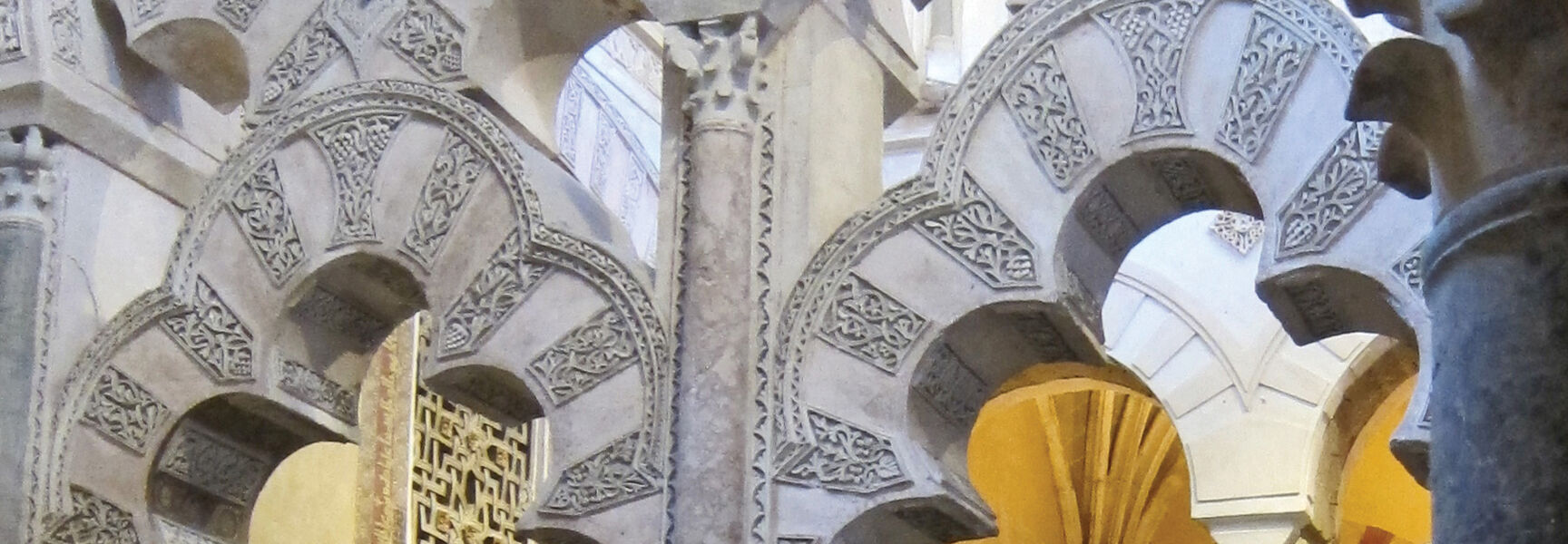 Intricate Moorish architecture in Spain featuring ornate multi-lobed stone arches with decorative carvings in a historic southern coast interior.