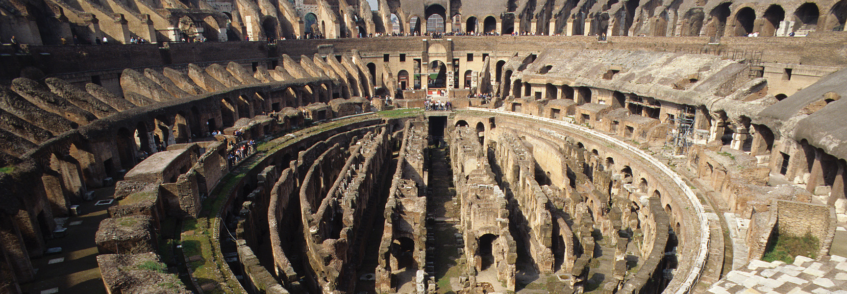 An overhead view of the ancient ruins inside the Colosseum in Rome, Italy, showing the exposed underground chambers and tiered seating.