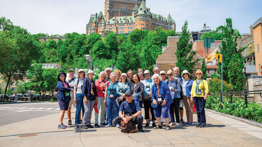 A large group of travelers poses for a photo in front of the iconic Fairmont Le Château Frontenac in Québec City.