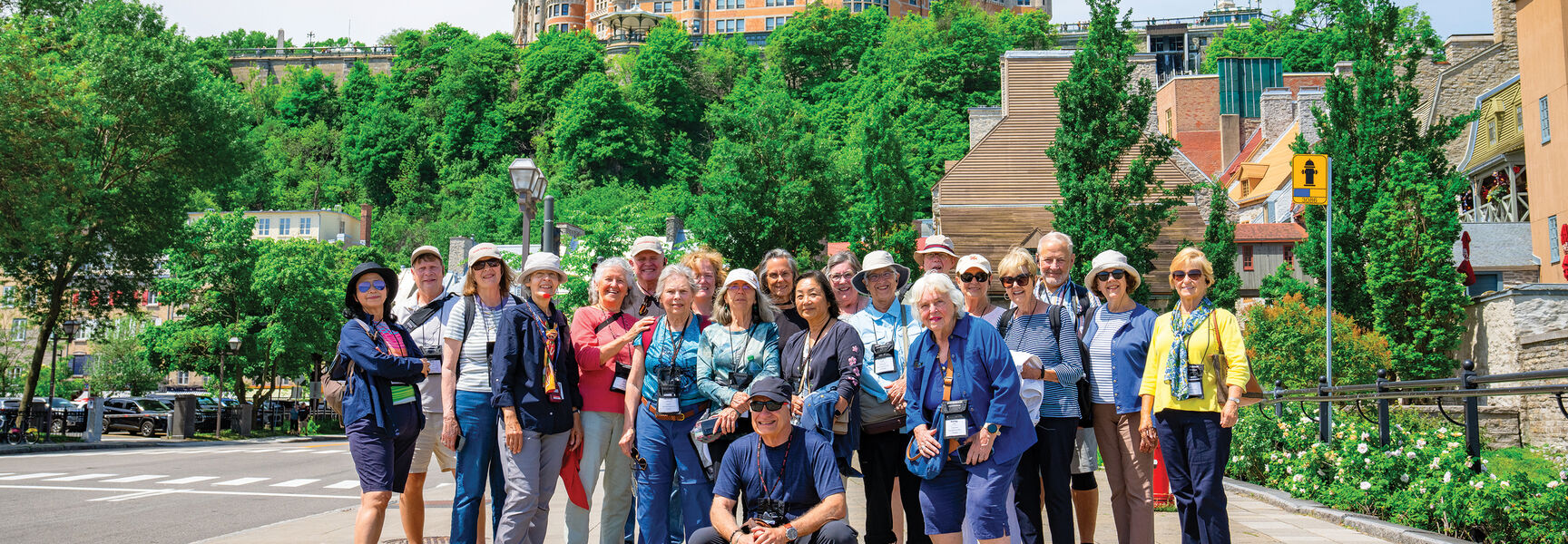 A large group of travelers poses for a photo in front of the iconic Fairmont Le Château Frontenac in Québec City.
