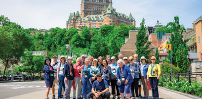 A large group of travelers poses for a photo in front of the iconic Fairmont Le Château Frontenac in Québec City.