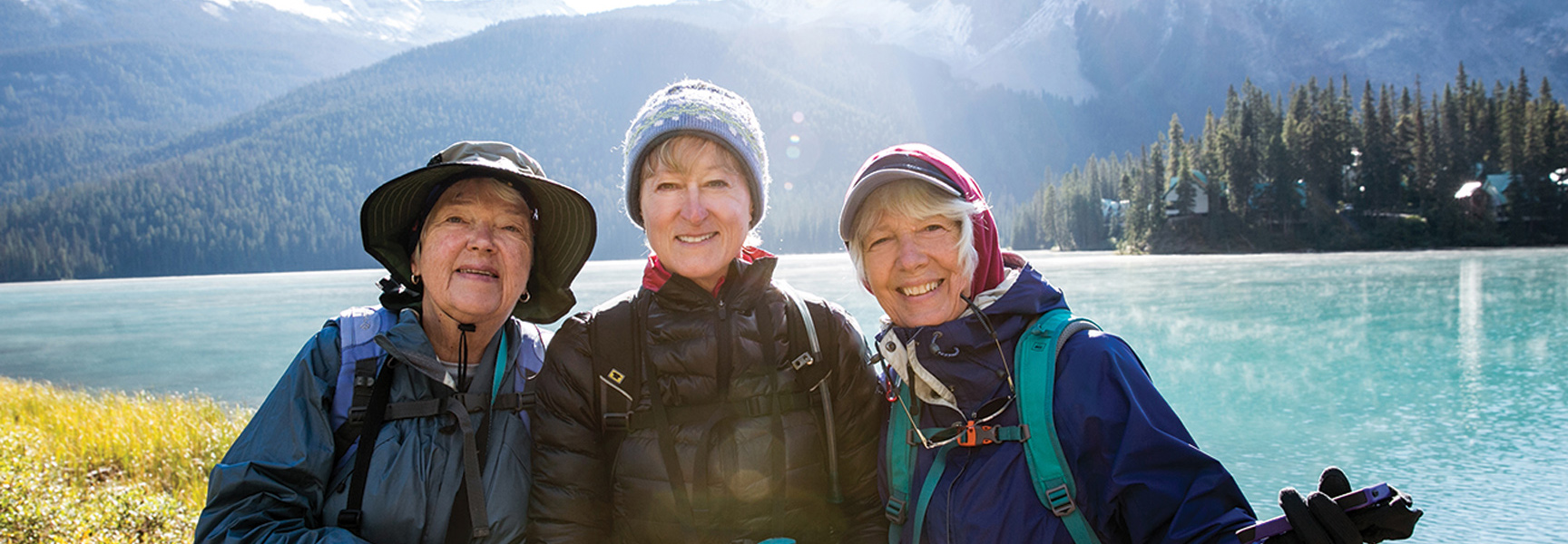 Three women in hiking gear smile in front of a bright blue lake and mountains in Banff, Alberta.