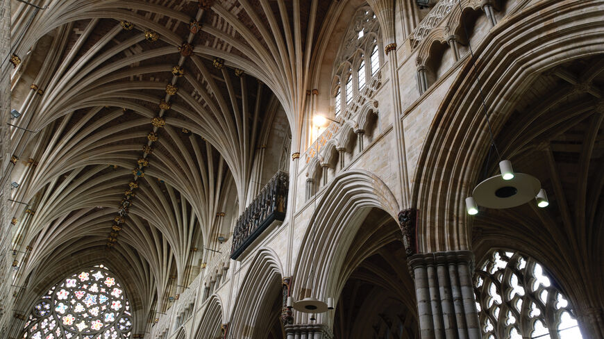 Ornate ribbed vaulting and a stained glass rose window inside a historic medieval cathedral in England.