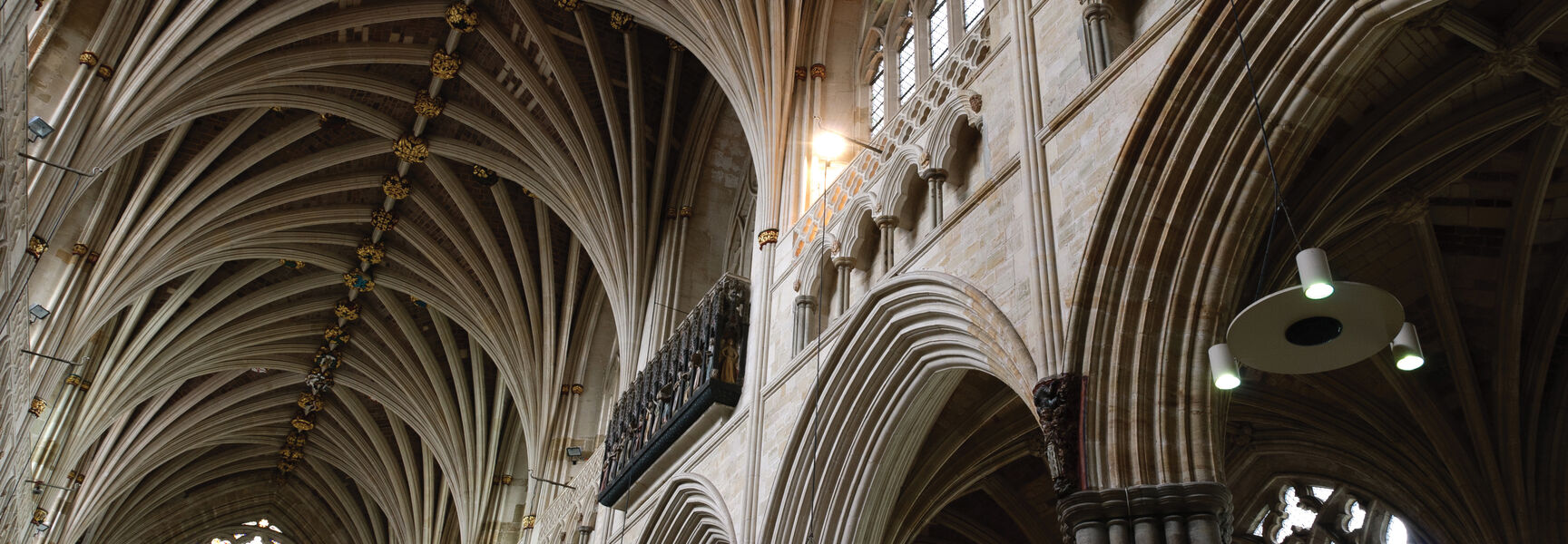 Ornate ribbed vaulting and a stained glass rose window inside a historic medieval cathedral in England.