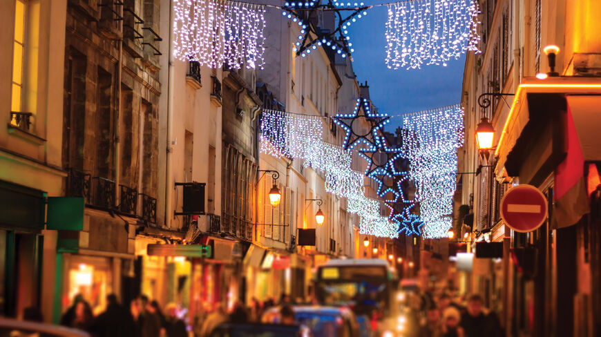 A street in Paris, France, illuminated with star-shaped festive lights and hanging decorations during a New Year's Eve celebration.