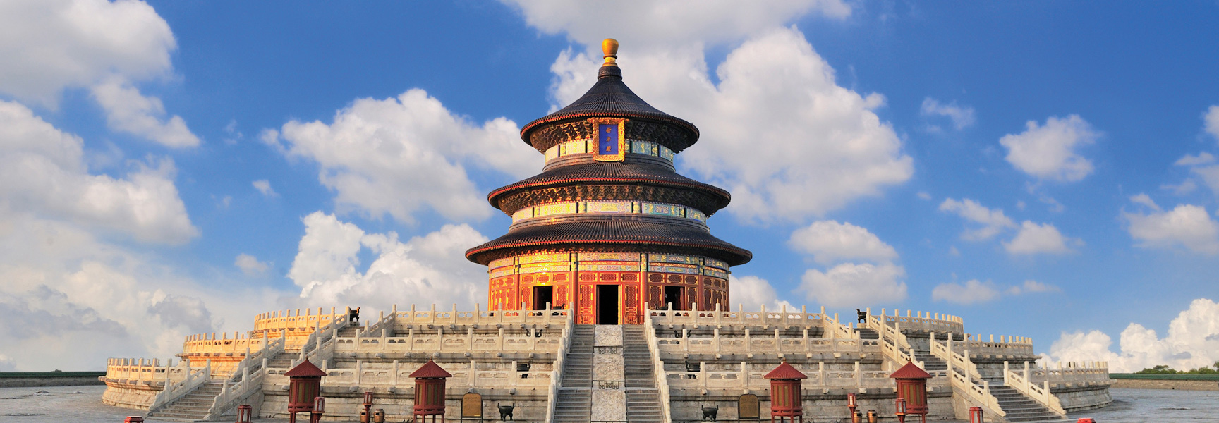 The iconic Temple of Heaven in Beijing, China, is a multi-tiered circular building on a stone terrace under a partly cloudy sky.