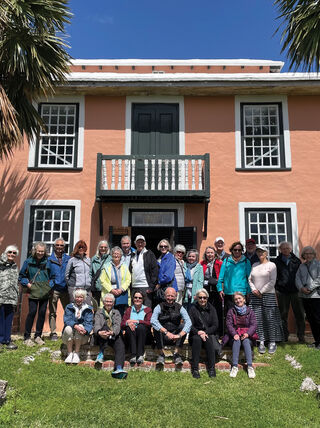 A group of travelers posing in front of a historic peach-colored building during a guided tour of Bermuda's cultural and historic sites.
