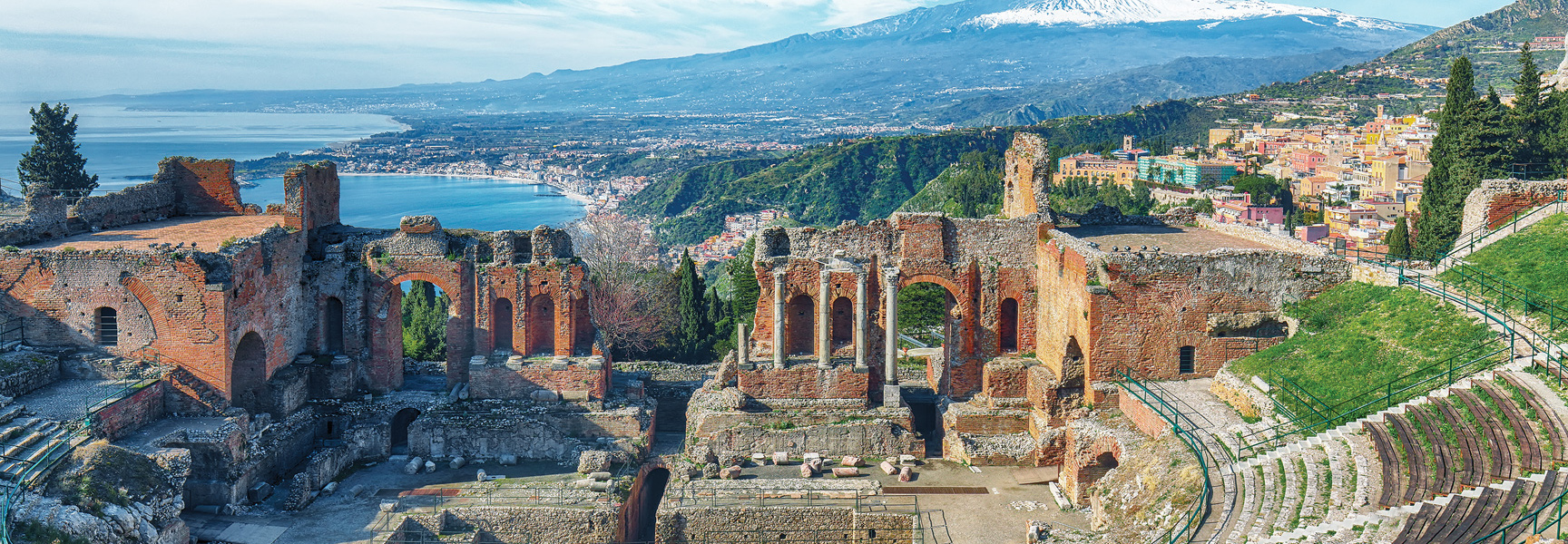 The ancient theatre ruins in Taormina, Italy, overlook the Ionian Sea with the snow-capped Mount Etna in the distance.