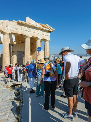 Tourists explore the secrets of ancient Greece as they stand before a monumental stone gateway during a tour of Classical Greece.