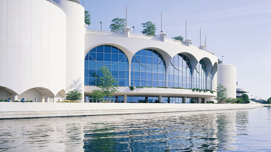 The white, arched exterior of Monona Terrace in Wisconsin, a Frank Lloyd Wright architectural masterpiece, reflected in the calm water.