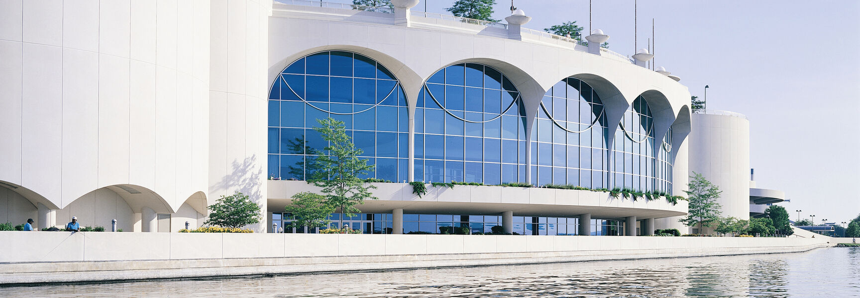 The white, arched exterior of Monona Terrace in Wisconsin, a Frank Lloyd Wright architectural masterpiece, reflected in the calm water.