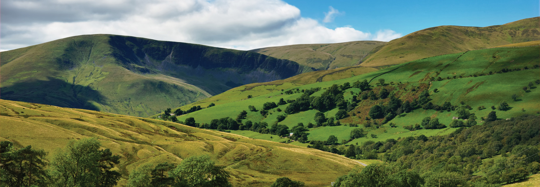 Rolling green hills and mountains of a national park in England under a blue sky with scattered white clouds.