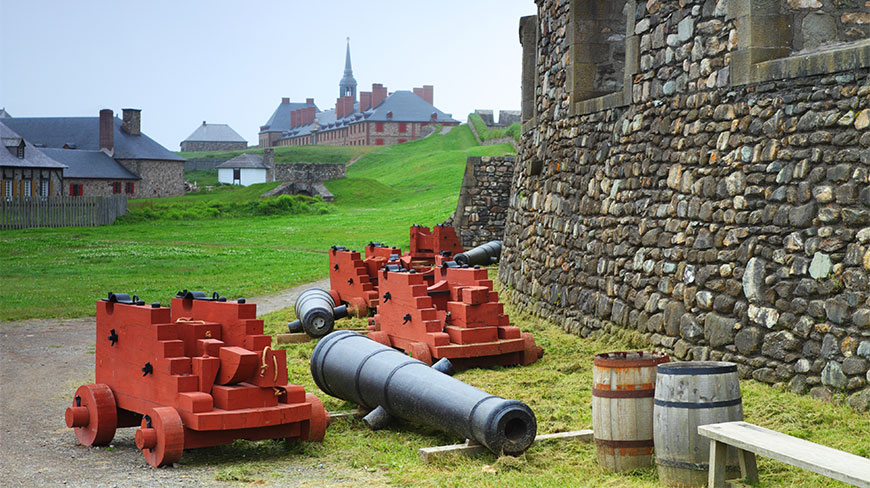 Historic black cannons and red wooden carriages sit on the grass beside a stone wall at the Fortress of Louisbourg in Nova Scotia.