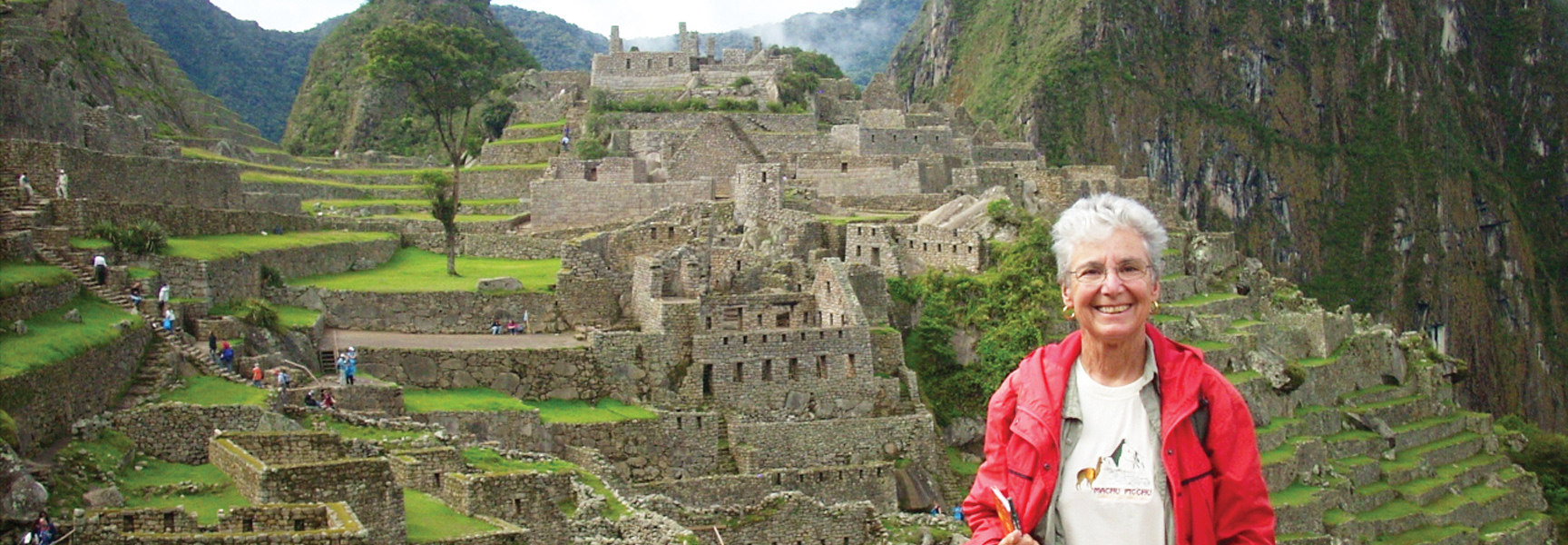 A woman in a red jacket smiles in front of the ancient stone ruins of Machu Picchu in Peru.