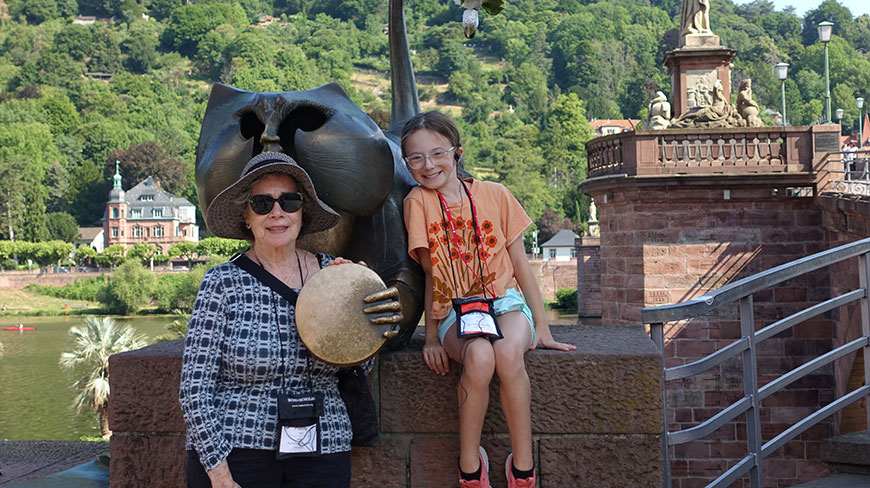 A grandmother and granddaughter pose with the Heidelberg Bridge Monkey statue in Germany.