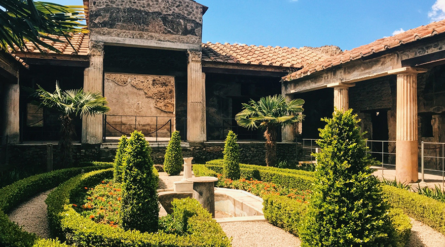 A sunny courtyard with a manicured garden sits within the ancient ruins of a Roman villa in Pompeii, Italy.