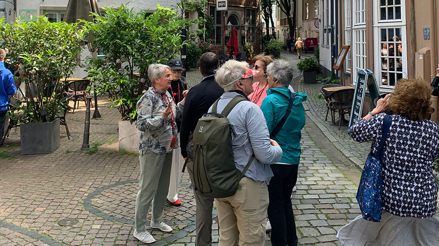 A group of travelers listens to a guide on a cobblestone street in the historic Schnoor Quarter of Bremen, Germany.