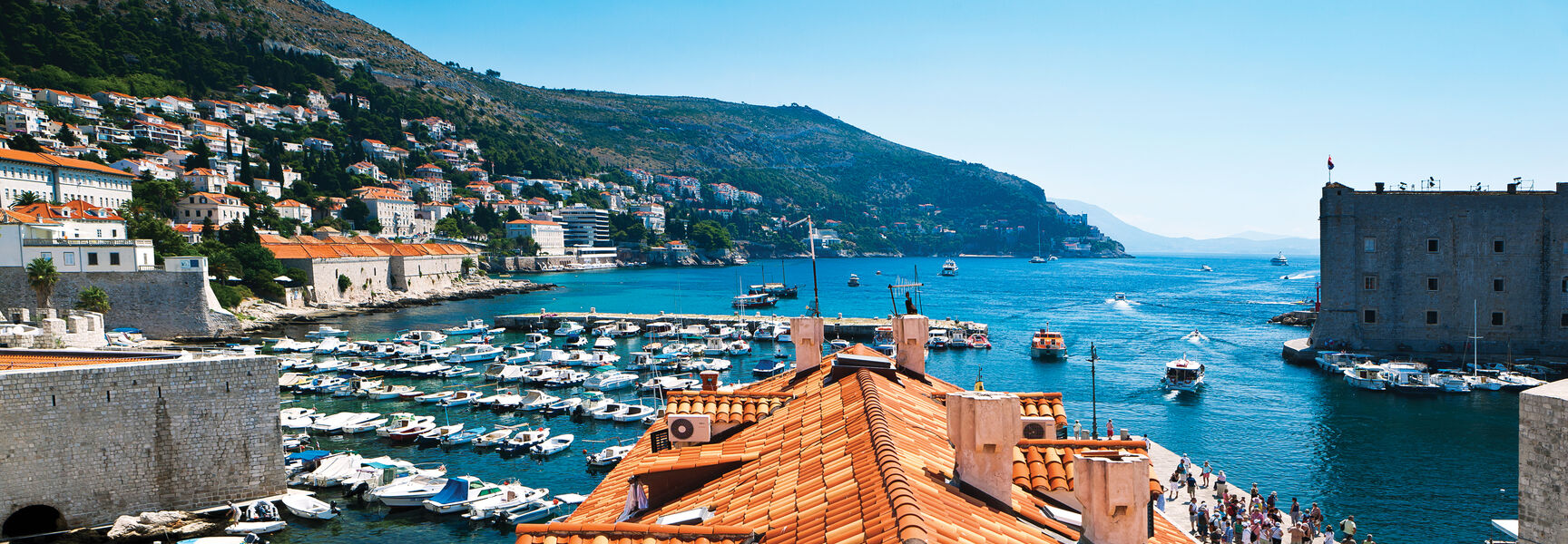 Terracotta-roofed buildings overlook a bustling harbor filled with boats in the historic coastal city of Dubrovnik, Croatia along the Dalmatian Coast.