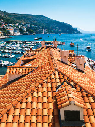Terracotta-roofed buildings overlook a bustling harbor filled with boats in the historic coastal city of Dubrovnik, Croatia along the Dalmatian Coast.