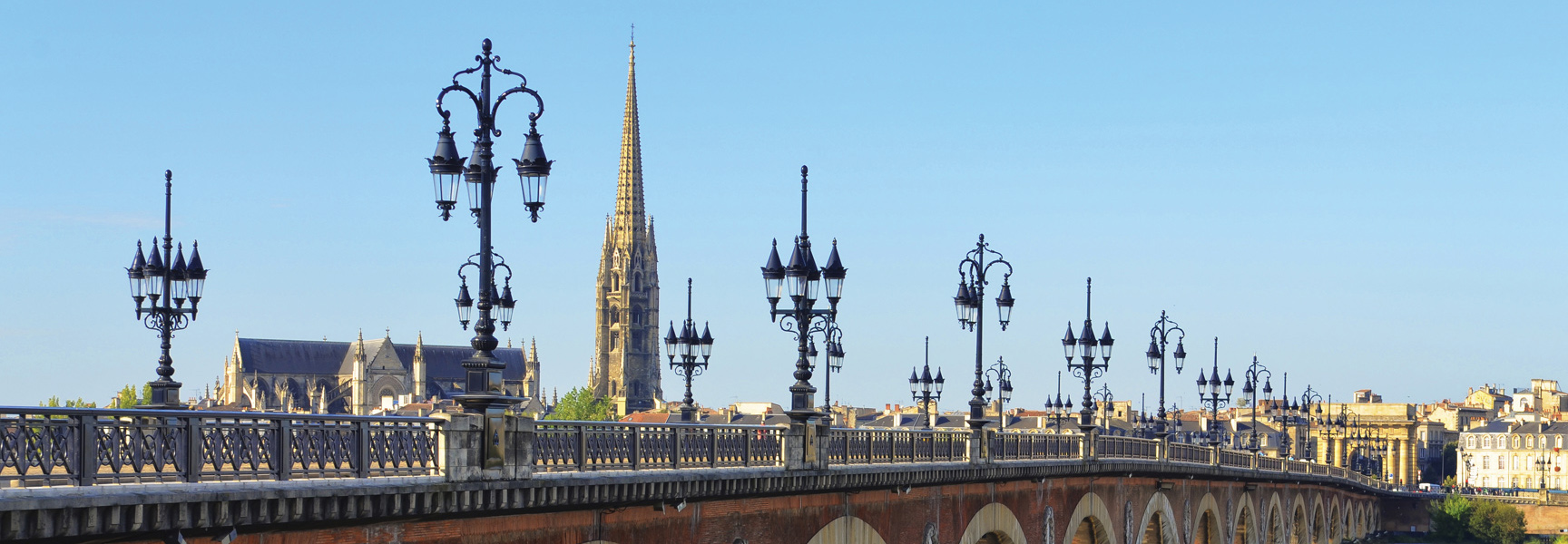 A scenic view of the Pont de pierre bridge with its ornate lampposts and the Basilica of St. Michael in the background in Bordeaux, France.