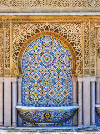 An ornate Moroccan wall fountain featuring intricate mosaic tilework and carved stonework arches showcasing the vibrant colors and traditional architectural crafts of Morocco.