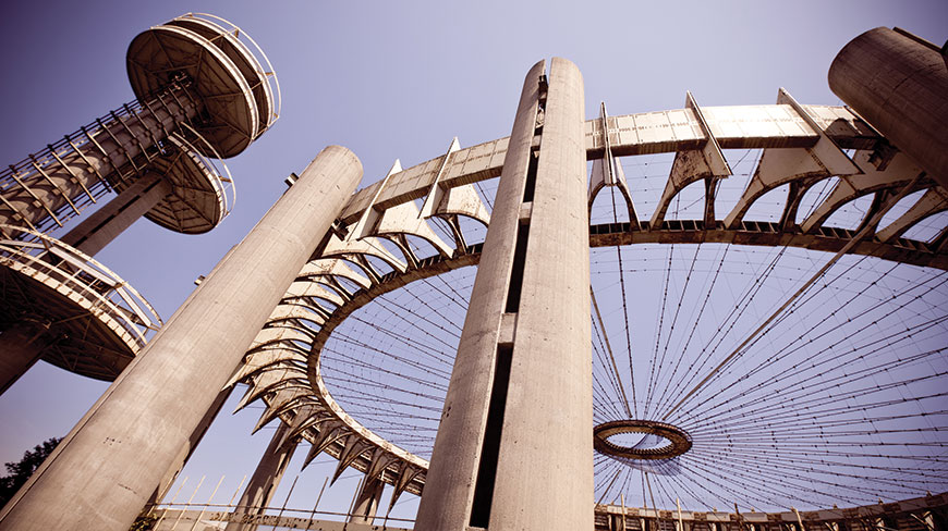A low-angle view of the futuristic, circular structures of the New York State Pavilion from the World's Fair against a clear blue sky.