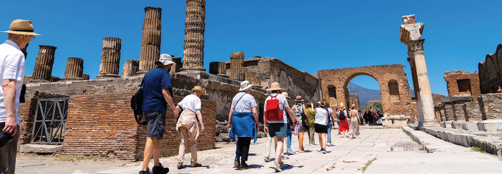 A group of travelers walks through sunny archaeological ruins with large stone columns on the Amalfi Coast, Italy.