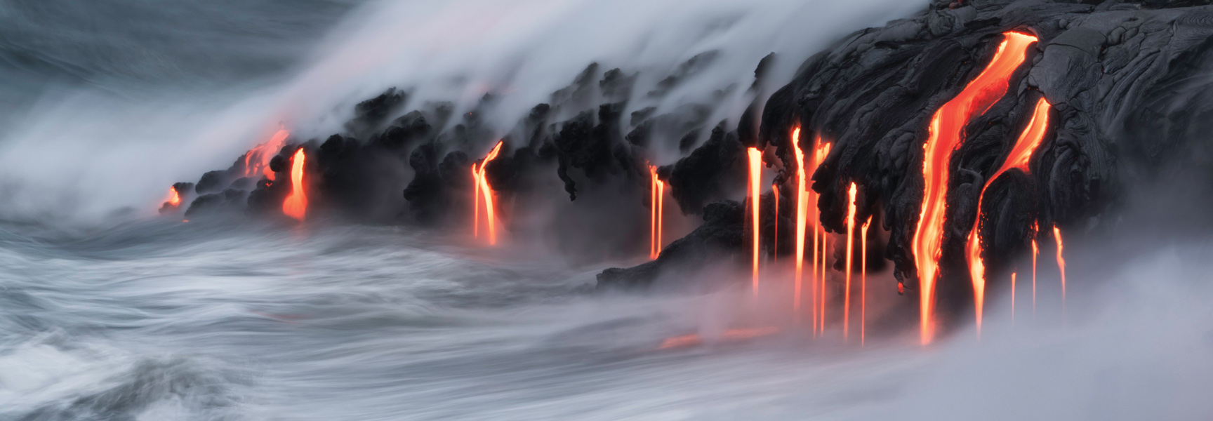 Molten lava streams down volcanic rock and into the misty, churning ocean on the Big Island of Hawaii.