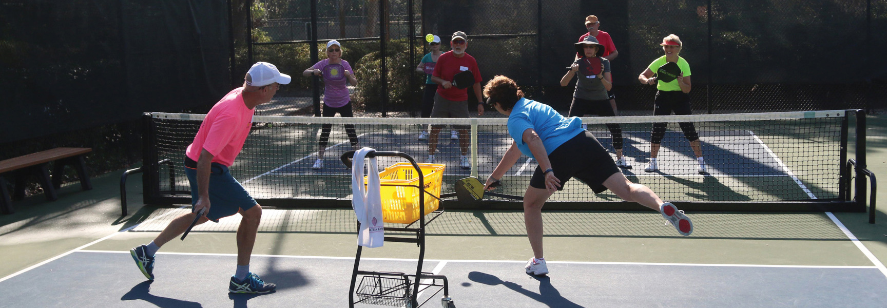 A group of people learn to play pickleball on a sunny outdoor court in Québec.