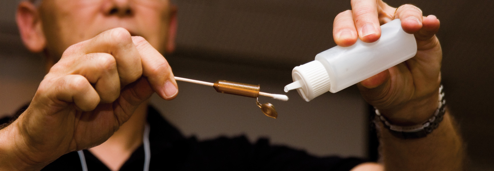 A forensics expert carefully swabs a bullet casing for evidence with a solution from a small plastic bottle.
