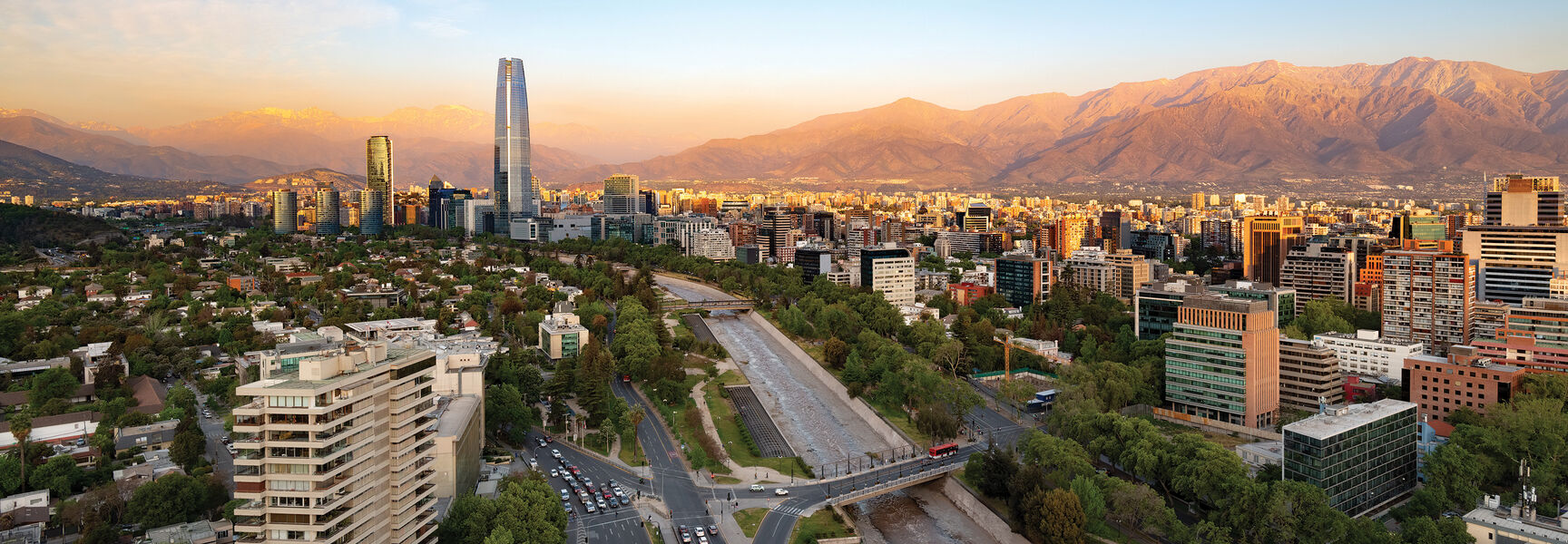 Aerial view of the Santiago, Chile city skyline at sunset, featuring the Gran Torre Santiago skyscraper and the Andes Mountains in the background.