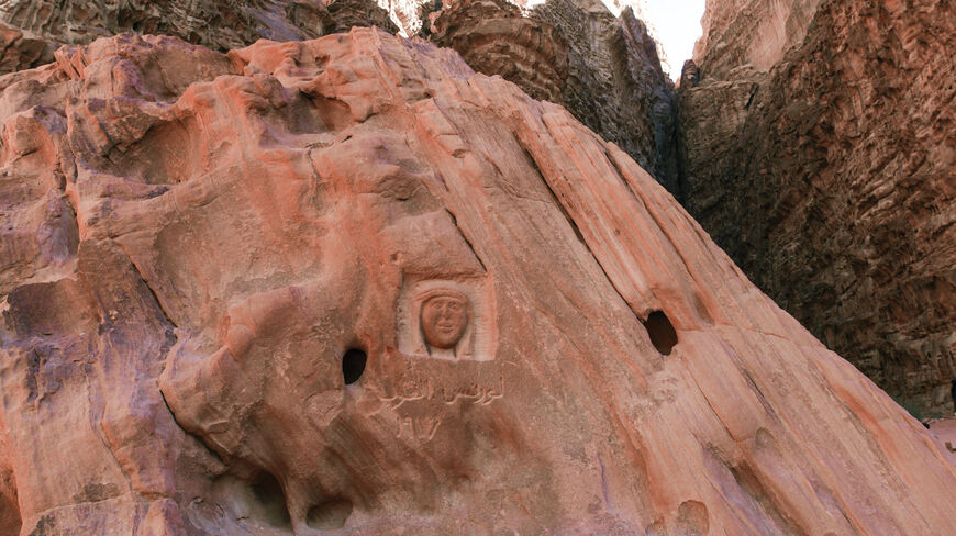 Carving of the face of Lawrence of Arabia and Arabic text on a red sandstone rock face in a desert canyon.
