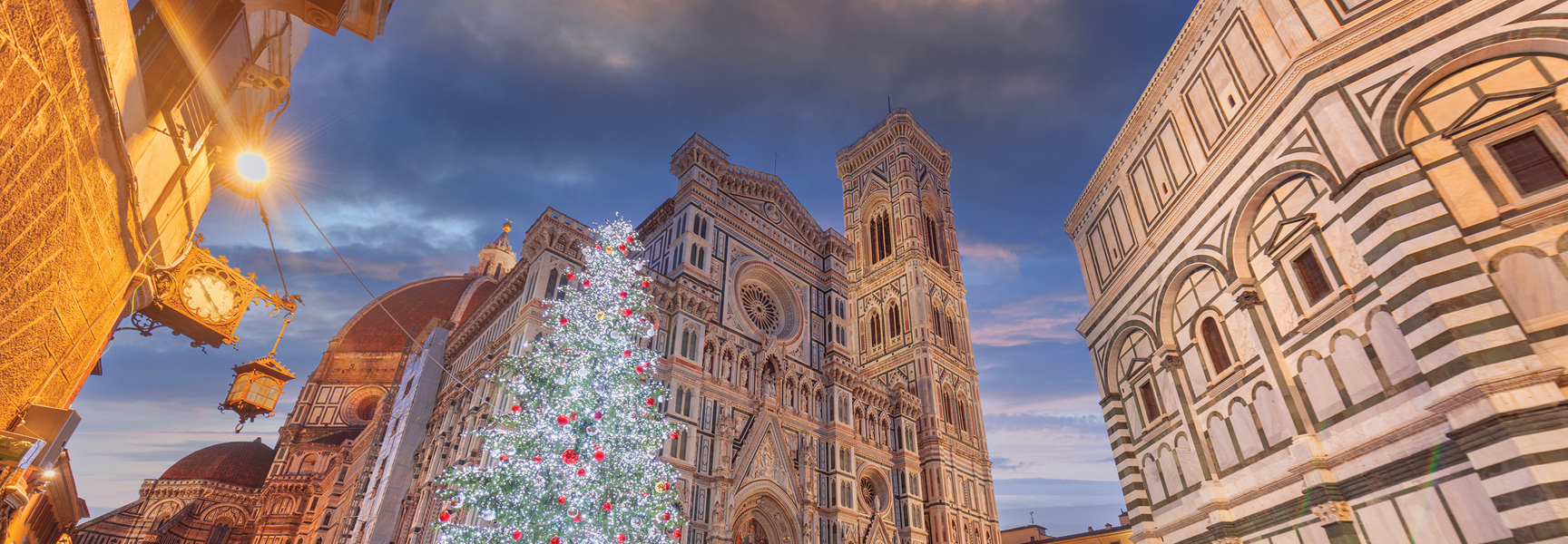 A large, illuminated Christmas tree stands in front of the Florence Cathedral in Italy at dusk.