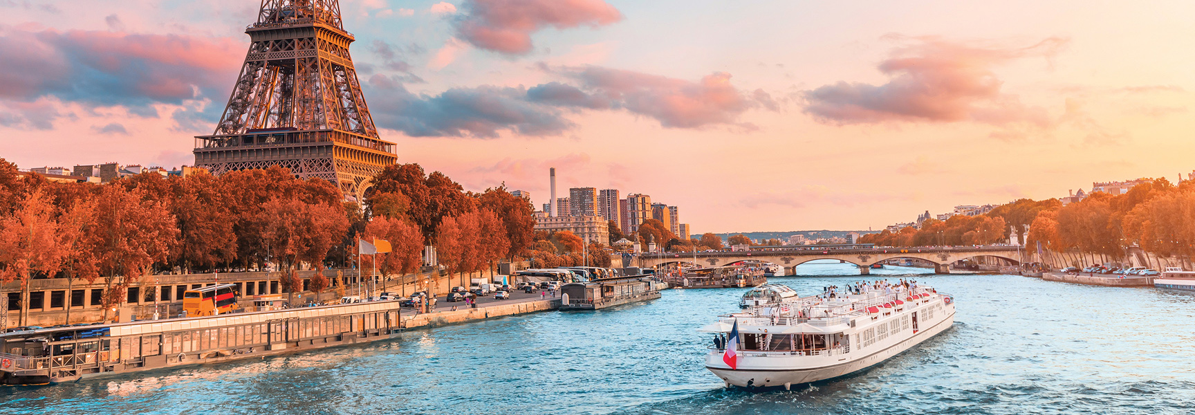 A tour boat on the Seine River in Paris, France, with the Eiffel Tower and colorful autumn trees during a beautiful sunset.