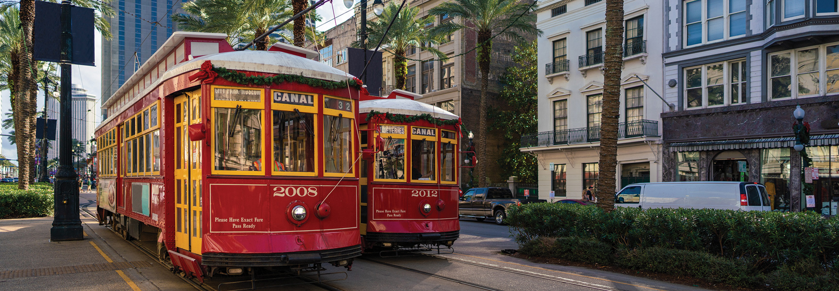 Two red Canal Street streetcars run along a track lined with palm trees and historic buildings in New Orleans, Louisiana.