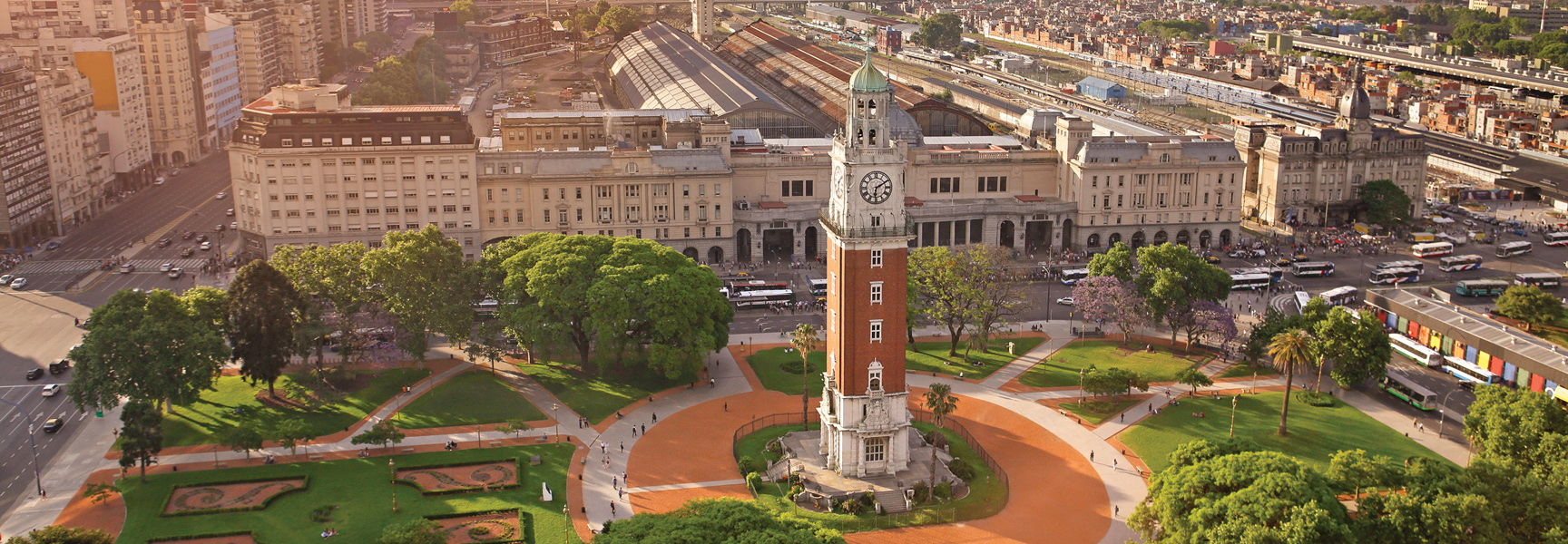 An aerial view of the Torre Monumental clock tower and a bustling city plaza in Buenos Aires, Argentina, during a sunny day.