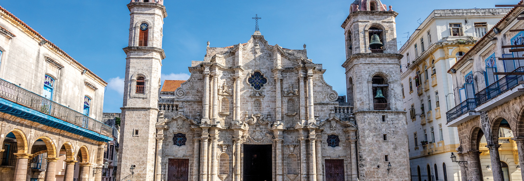 An ornate stone cathedral with two bell towers stands in a sunny plaza in Havana, Cuba.