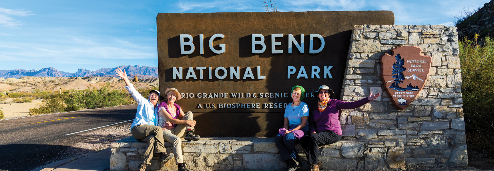 Four women smile for a photo at the entrance sign for Big Bend National Park in the Texas desert landscape.