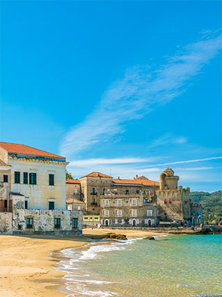The historic waterfront and sandy beach of Santa Maria di Castellabate in Italy under a bright blue sky.