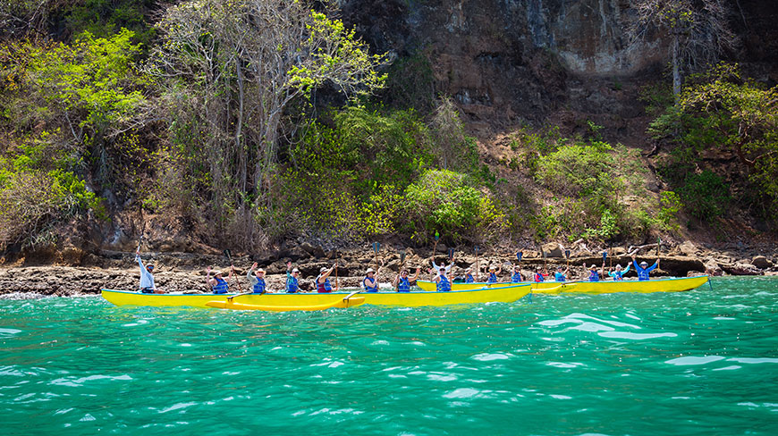 A group of travelers waves from two yellow outrigger canoes on the turquoise sea along the coast of Costa Rica.