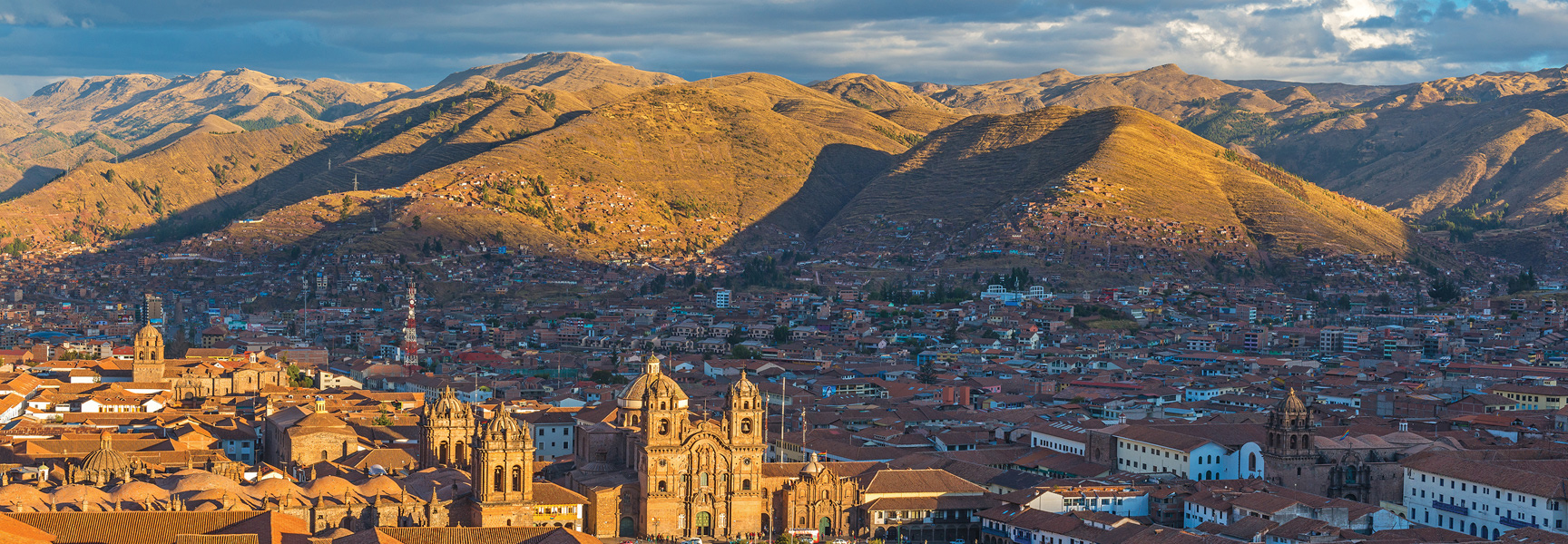 A sprawling city with red-tiled roofs nestled in a sunlit mountain valley in Peru.