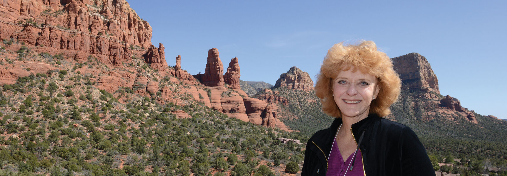 A smiling woman holding a camera stands before the iconic red rocks of Sedona, Arizona, during a Red Rock Country tour.