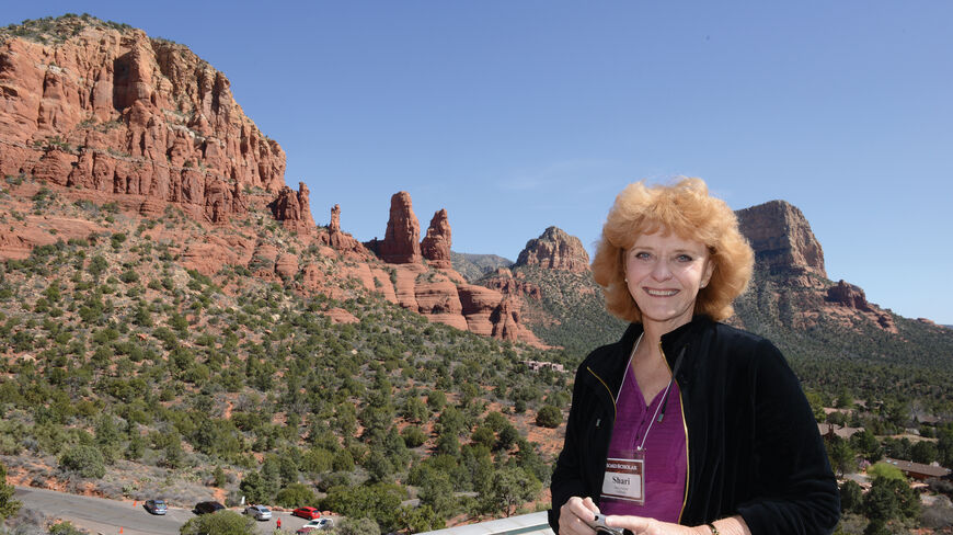 A smiling woman holding a camera stands before the iconic red rocks of Sedona, Arizona, during a Red Rock Country tour.