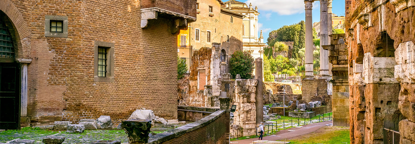 Ancient Roman ruins and historic brick buildings within the Rome Jewish Ghetto archaeological area under a sunny blue sky.