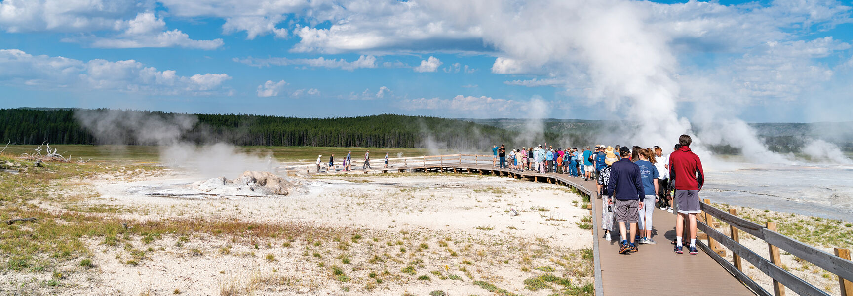 A group of travelers explore a steaming thermal basin from a boardwalk during an active adventure in Yellowstone National Park.