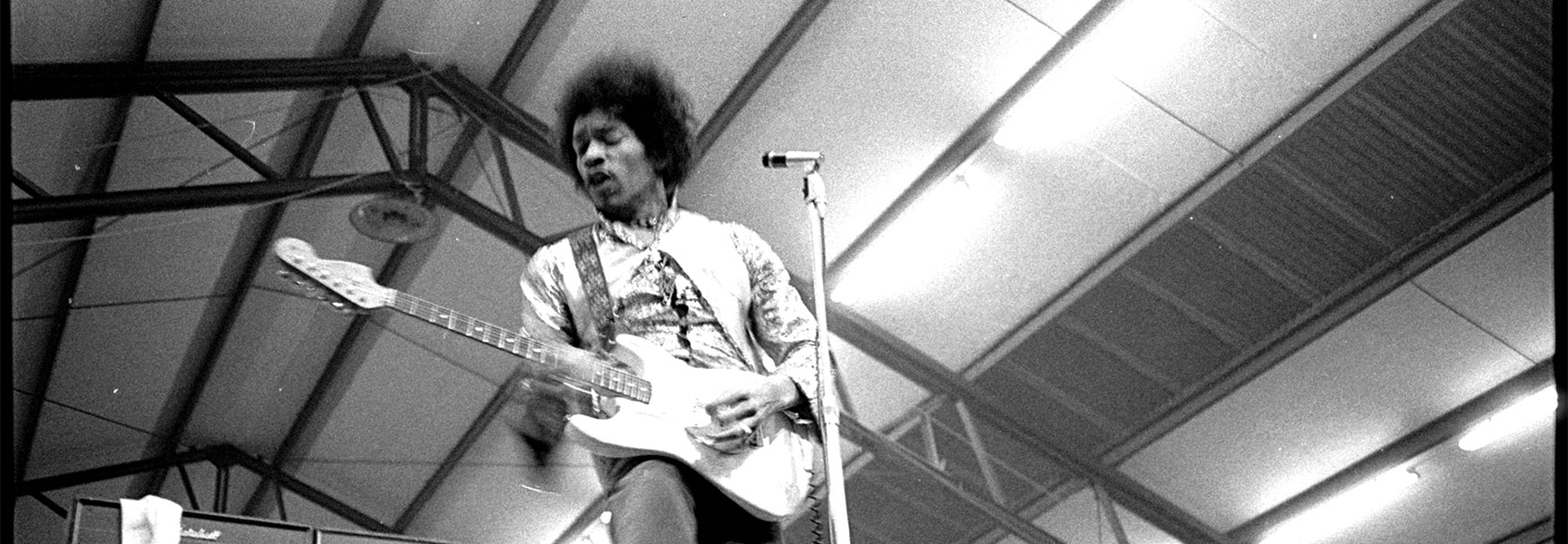 Black and white photograph of Jimi Hendrix playing a white electric guitar on stage during the Monterey Pop Festival.